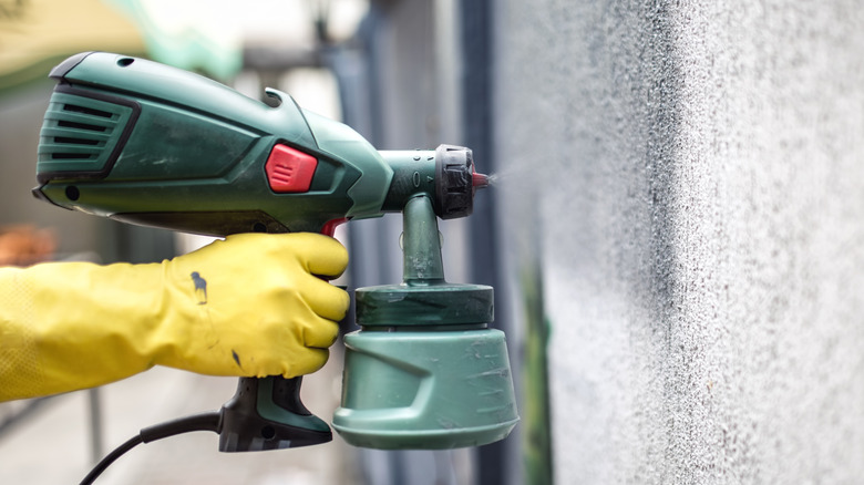 A gloved hand using an airless paint sprayer on a wall