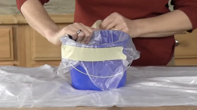 A lady taping a plastic liner in a blue bucket