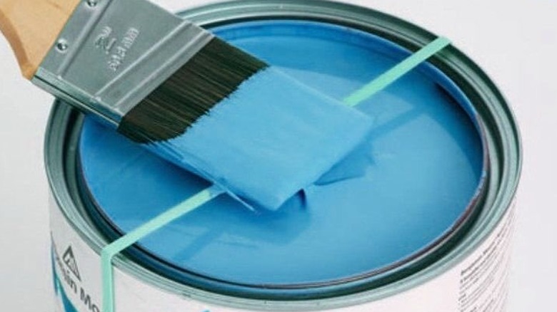 Blue paint being wiped off a paint brush with a rubber band