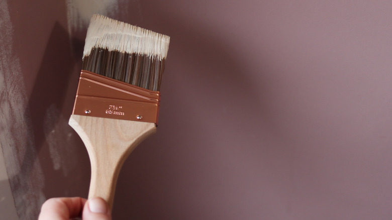 Angled paintbrush painting cream on a purple wall