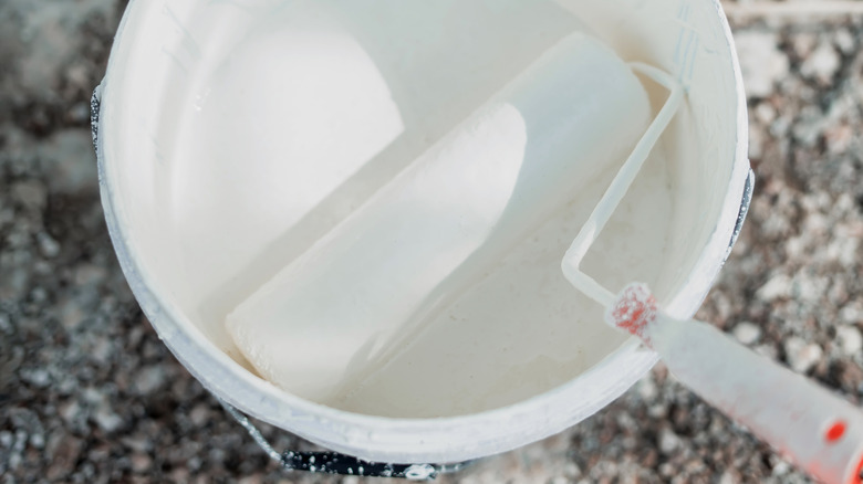 A paint bucket with white paint and a roller