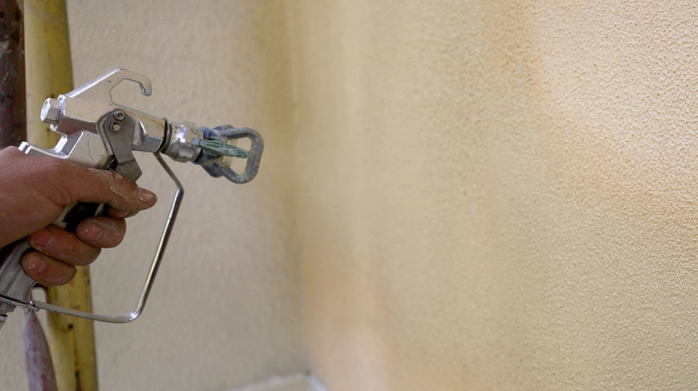 A hand using an airless paint sprayer on a wall