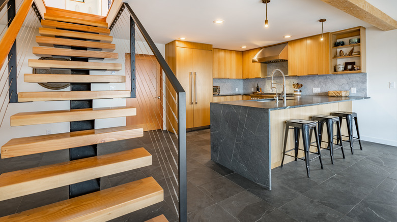 An open kitchen with gray slate floors, a marbled gray island, and wooden cabinetry
