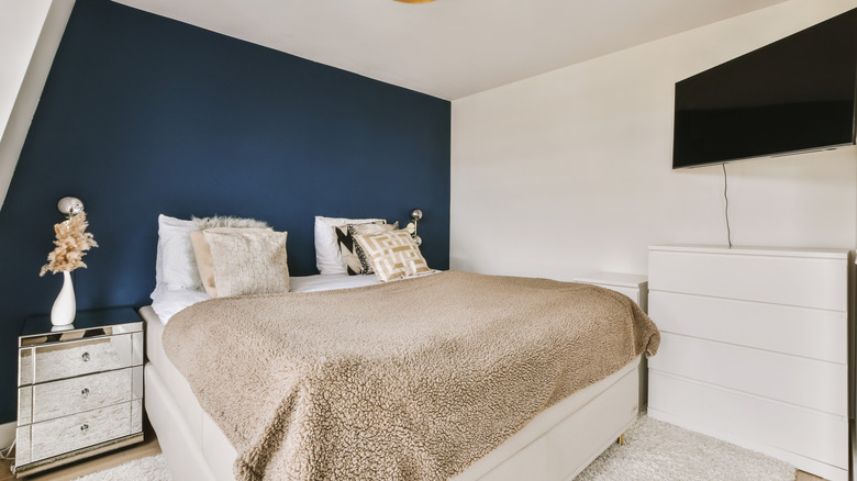 A dark blue wall behind a bed in a small bedroom