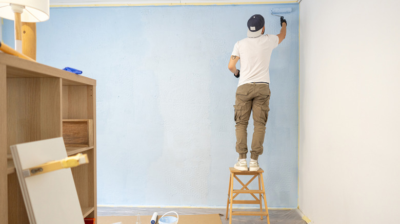 Man standing on stool and painting a wall light blue