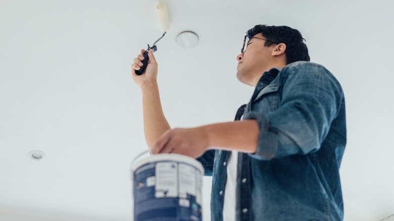 Man painting a ceiling white in a grey-walled room