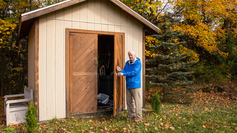Older man holding open the door of a garden shed