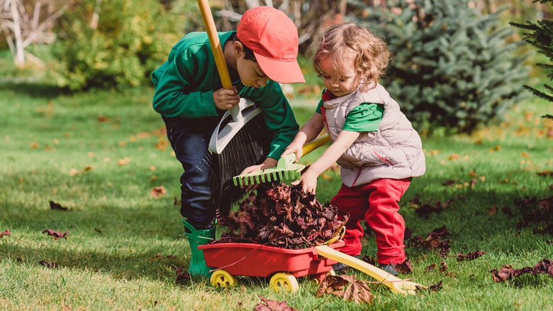 Two children racking leaves into a plastic wagon