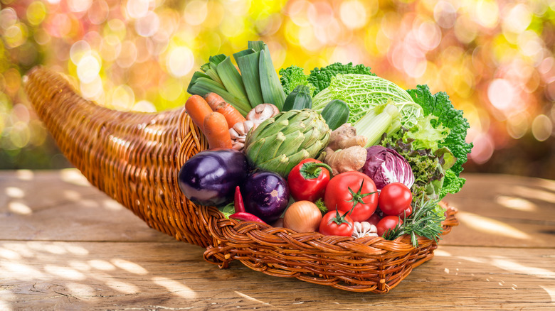 A cornucopia outside stuffed with produce like eggplants, artichokes, greens, onions, zucchini, tomatoes, onions, and more