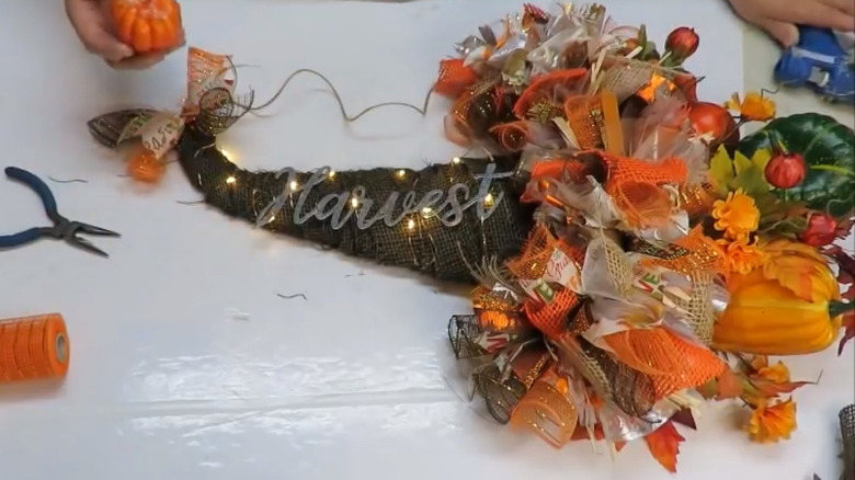 A cornucopia filled with ribbons, small pumpkins, fake flowers, lights, and a sign saying 'harvest'