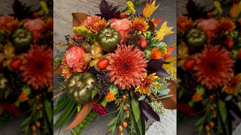 A cornucopia filled with flowers, fall leaves, greenery, and a few metallic pumpkins