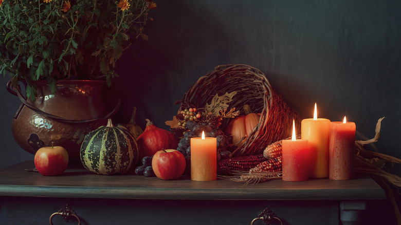 A cornucopia overflowing on a side table surrounded by candles