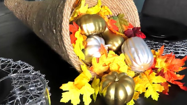 A cornucopia filled with faux flowers and metallic pumpkins