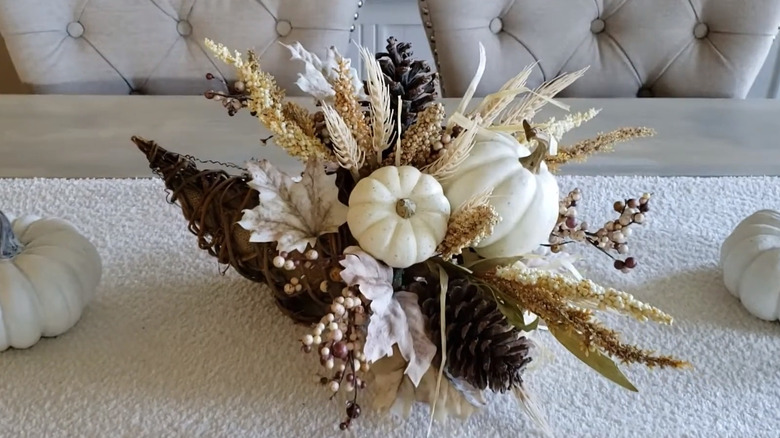 A cornucopia with white pumpkins, pine cones, and neutral-colored plants