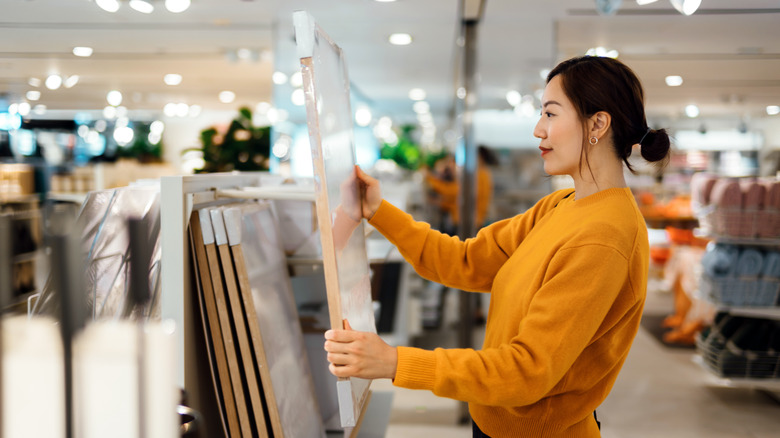 woman holding and looking at framed artwork in store