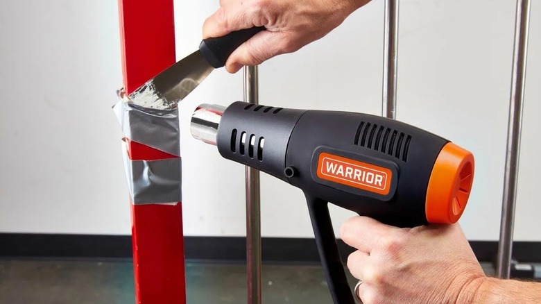 Person aiming a heat gun at duct tape on a metal beam