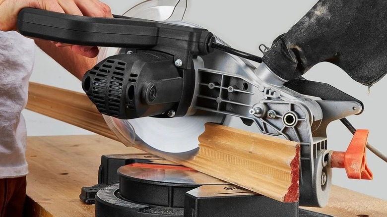 Person using a small miter saw on a piece of wood molding