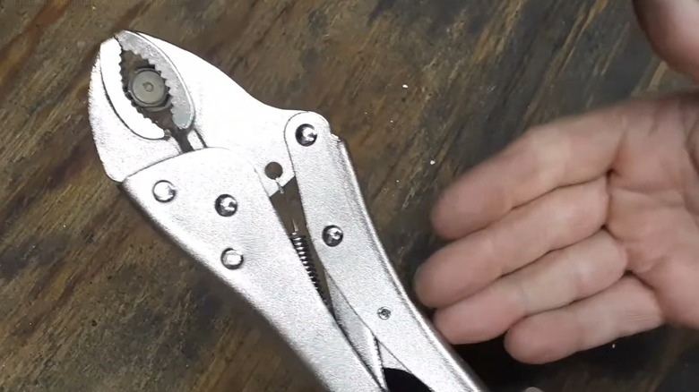 Hand pointing to locking pliers on a wooden table