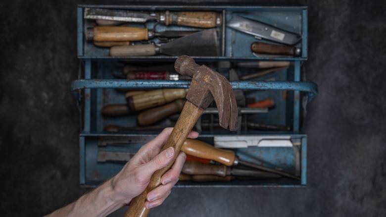 hand lifting hammer out of old metal toolbox filled with tools