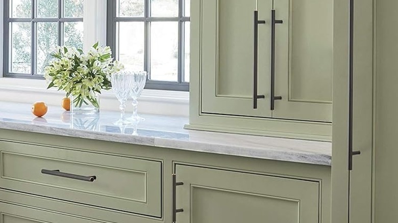 A close-up of light green cabinets with brown metal handle pulls.