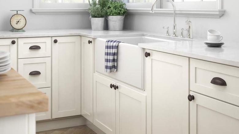 A close-up of while kitchen cabinets with brown cabinet pulls and knobs.