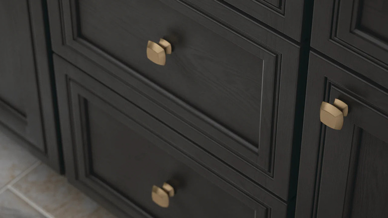 A close-up of dark brown cabinets with gold square knobs.