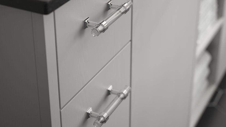 A close-up of acrylic cabinet pulls installed on grey cabinets.