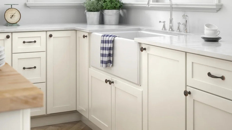 A close-up of white kitchen cabinets with brown metal handle pulls and knobs.