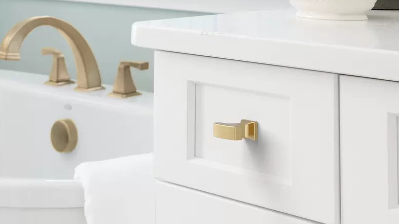 A close-up of white bathroom cabinets with gold hardware.