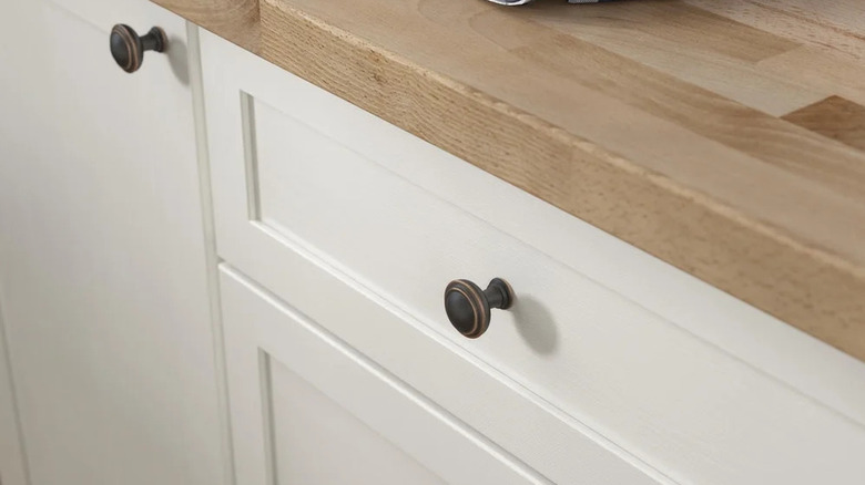 A close-up of white kitchen cabinets with bronze knobs