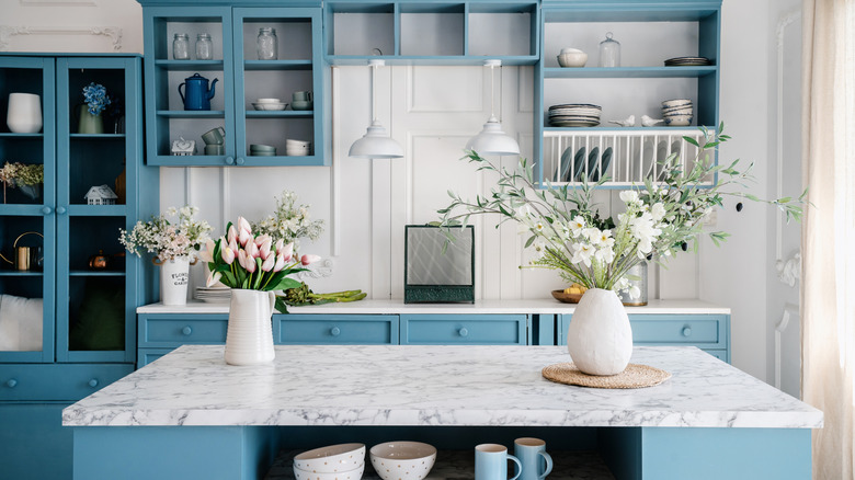A blue-green and white kitchen with flowers on island.