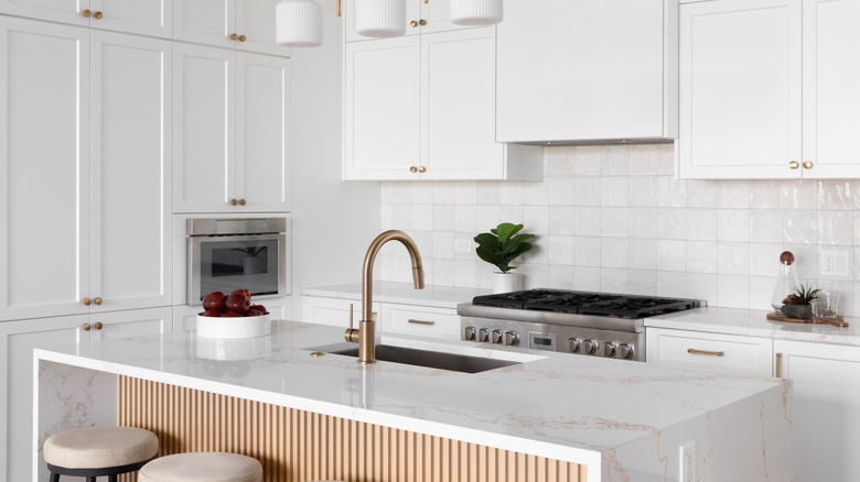 An all white kitchen with an island and gold fixtures.