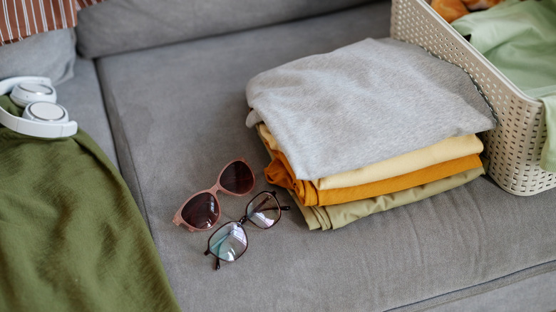 Pile of clothes and sunglasses on a grey couch