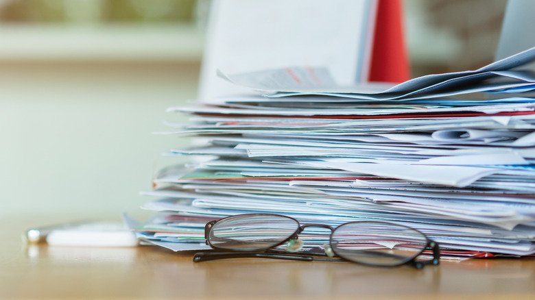 Stack of papers near a board and pair of eyeglasses