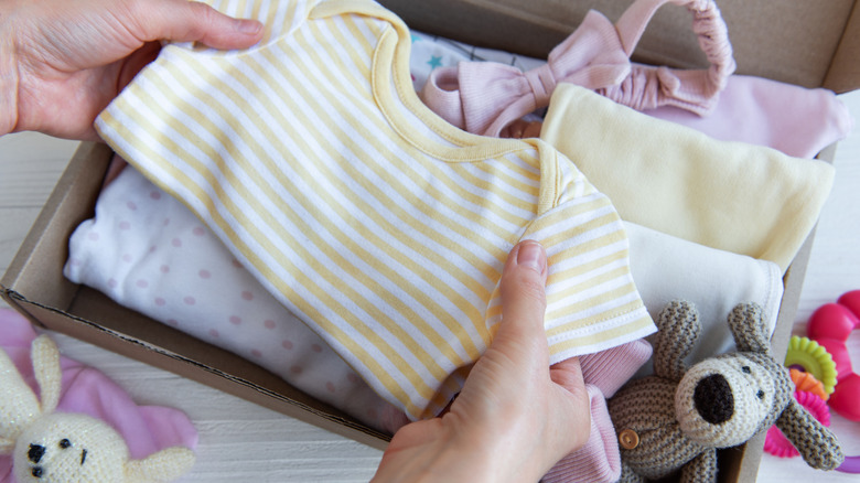 Person folding up children's clothing in a box, a pink headband bow and polka dotted shirt among them, along with a small crocheted dog