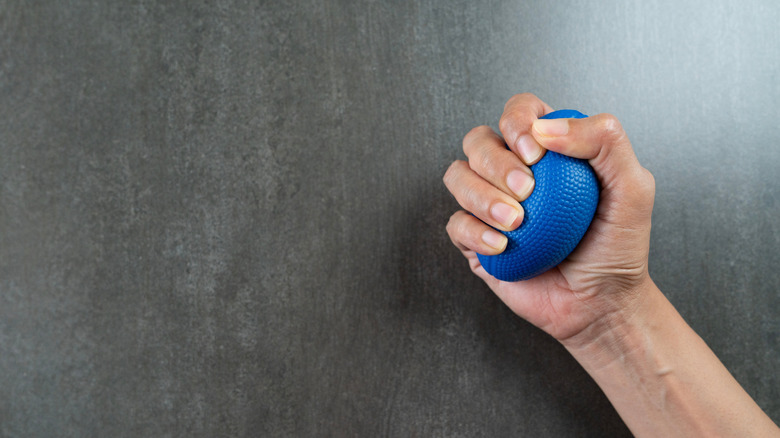 Hand squeezing blue stress ball against a dark background