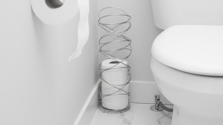 decorative metal toilet paper basket holding rolls beside toilet
