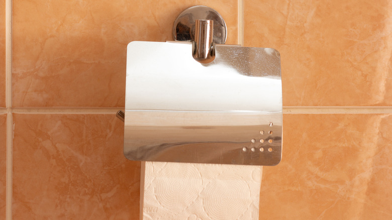 unraveled toilet paper hanging from wall mount with metal flap