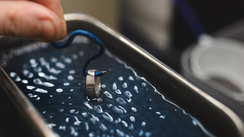 Person putting a ring inside the tank of an ultrasonic jewelry cleaner