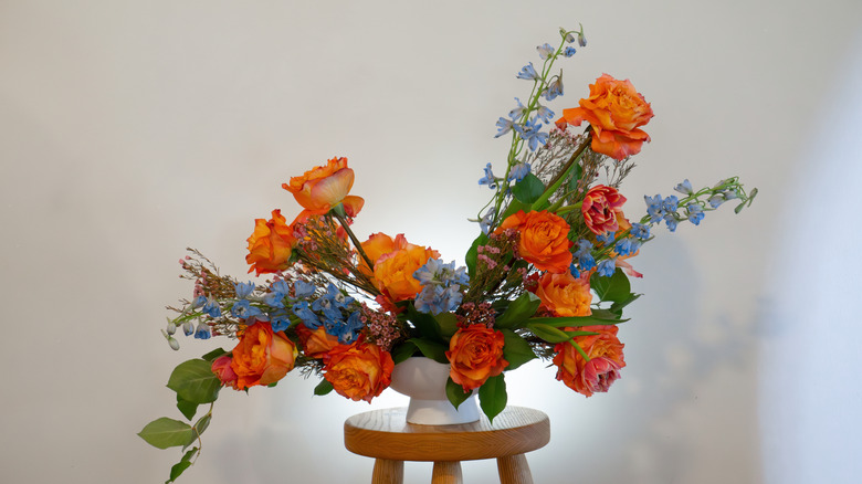 Orange roses, delphinium, and other flowers and foliage make up an asymmetrical bouquet.