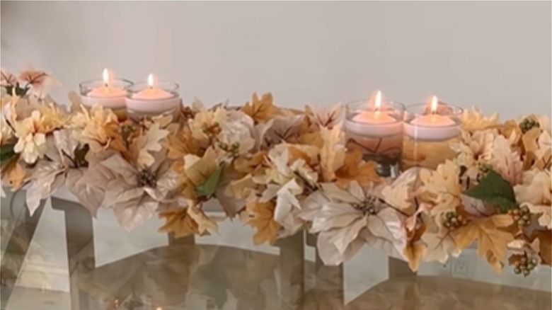 A runner of cream and beige faux flowers and vases with candles is made from Dollar Tree purchases.