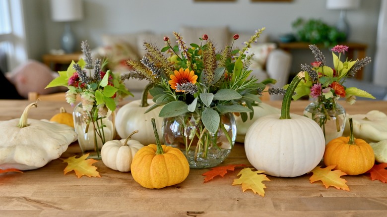 A trio of clear vases hold cut flowers and are surrounded by squash.
