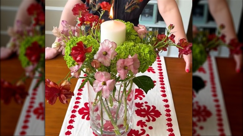 An inverted wine glass inside a vase holds a candle while the vase contains a bouquet.