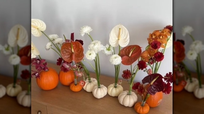 Long-stemmed flowers stand in small pumpkins as vases.