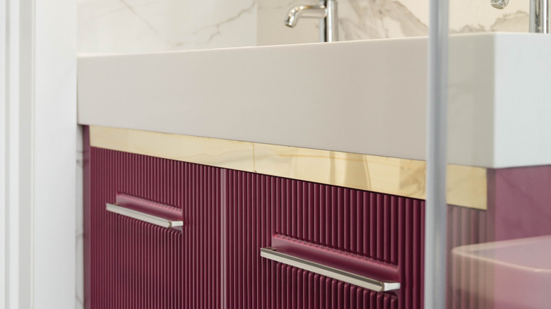 A bathroom sink with fluted purple cabinets.