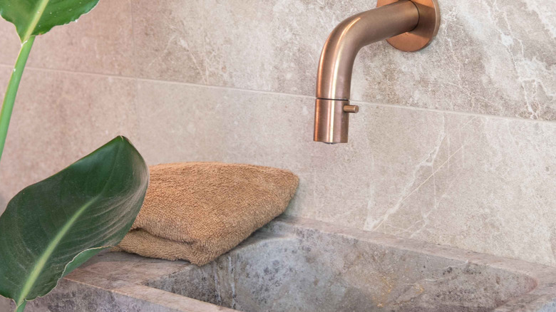 A close up on a stone sink with a copper faucet.