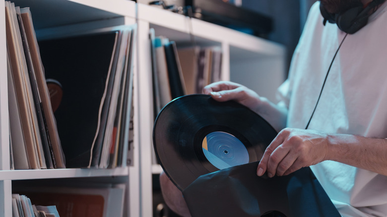 A person takes a record out of its sleeve in front of a bench repurposed to store vinyl and a record player.