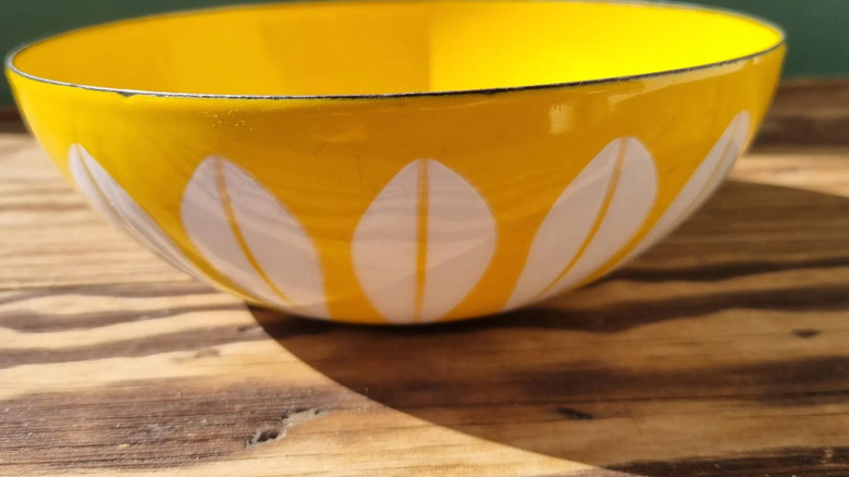 A bright yellow Catherineholm Lotus Enamel Bowl sits on a wooden table