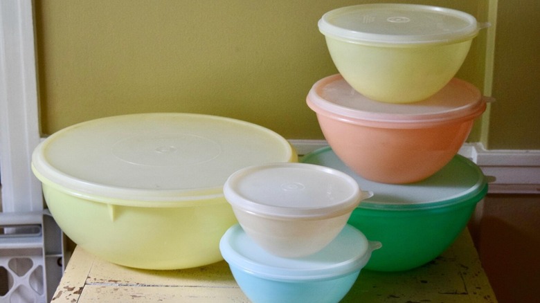 A collection of vintage pastel Tupperware bowls sits on a distressed wooden table