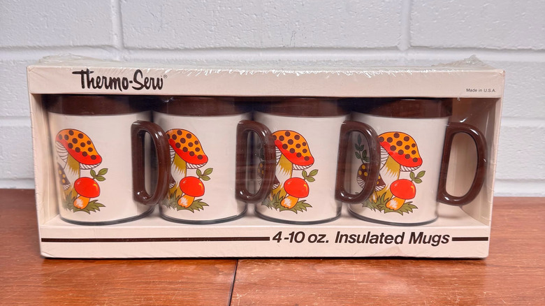 A set of Thermo-Serv Merry Mushroom Insulated Mugs in their original packaging sit on a table